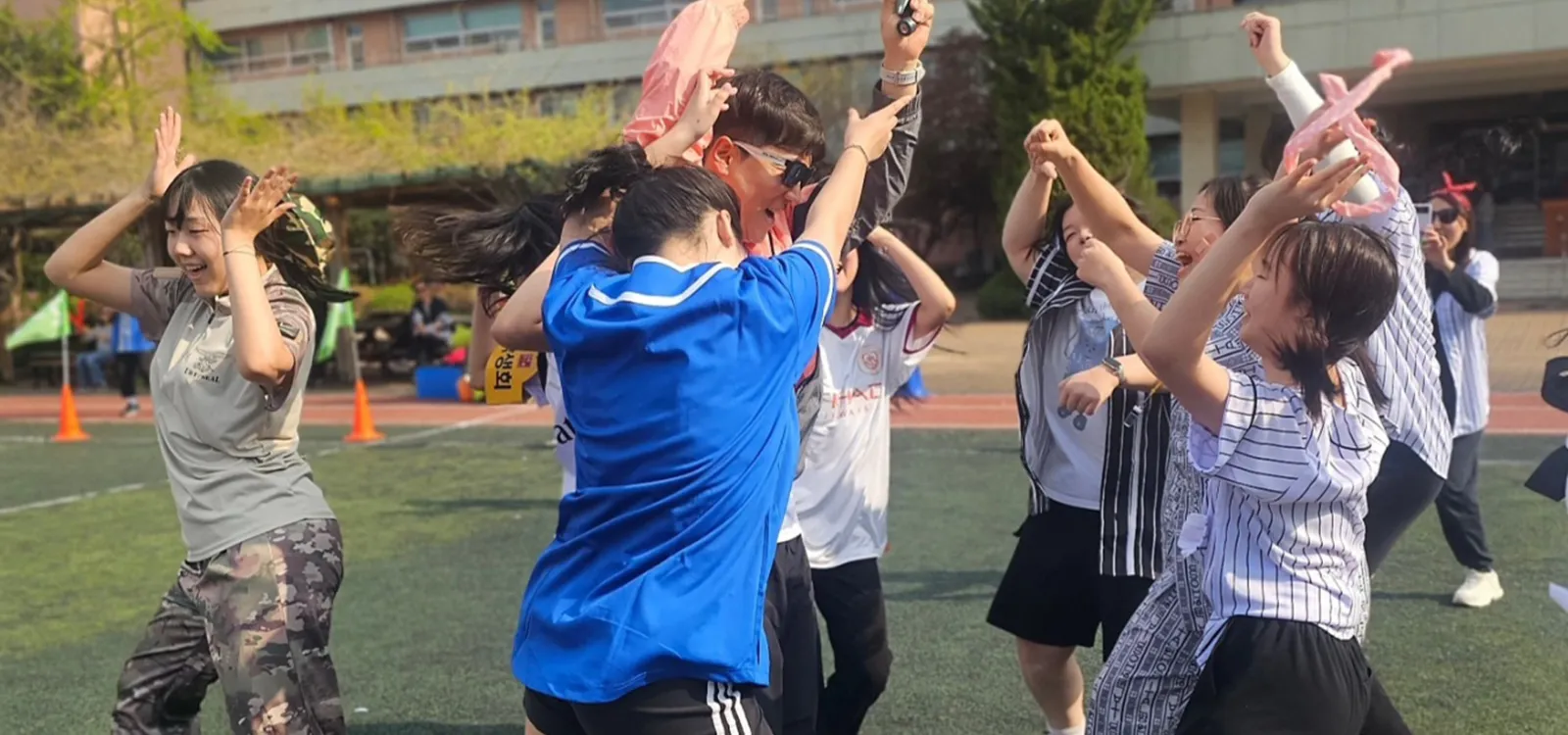 학교 운동장에서 참가자들이 팔을 들고 함께 몸을 푸는 체육대회 장면