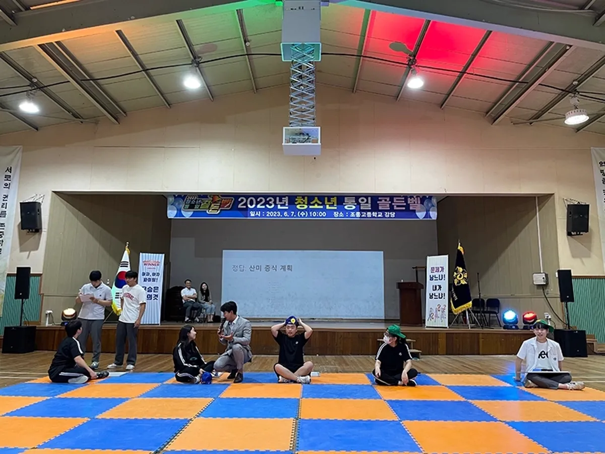 체육관 바닥에 체크무늬 매트를 깔고 무대 앞에서 진행하는 실내 행사 장면